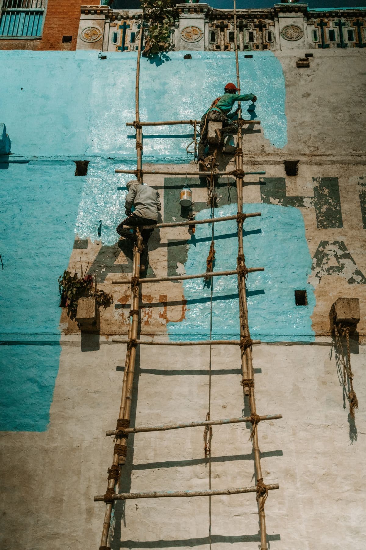 Painters on a bamboo ladder painting a building wall